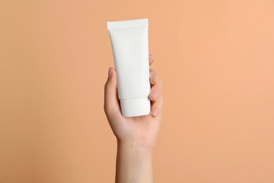 Woman holding tube of face cream on coral background, closeup