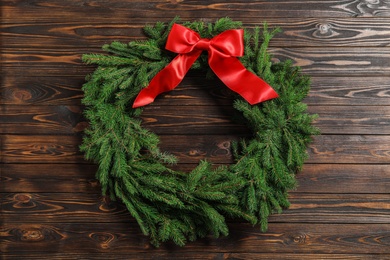 Christmas wreath made of fir branches with red bow on wooden background