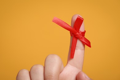 Man showing index finger with red tied bow as reminder on orange background, closeup
