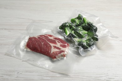 Raw beef and broccoli in vacuum packs on white wooden table