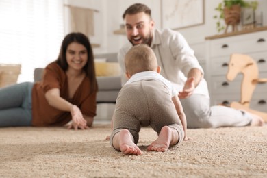 Photo of Happy parents watching their baby crawl on floor at home