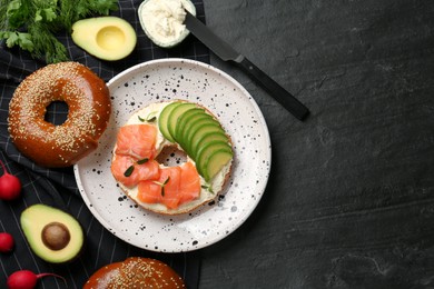 Photo of Delicious bagel with cream cheese, salmon and avocado on black table, flat lay. Space for text