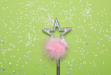 Beautiful silver magic wand with feather and confetti on light green background, flat lay