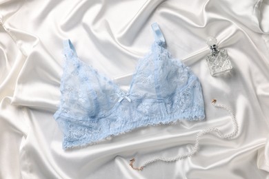 Photo of Light blue women's underwear, perfume and necklace on white fabric, flat lay