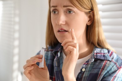 Photo of Upset woman with herpes applying cream on lips indoors