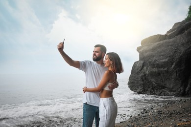 Happy young couple taking selfie on beach near sea
