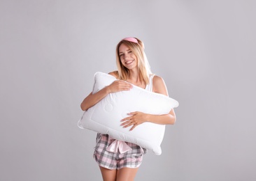 Young woman in pajamas embracing pillow on gray background