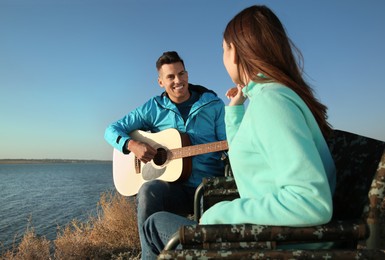 Photo of Couple with guitar resting in camping chairs near river on sunny day