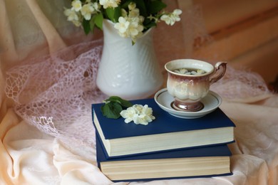 Cup of aromatic tea, beautiful jasmine flowers and books on fabric indoors