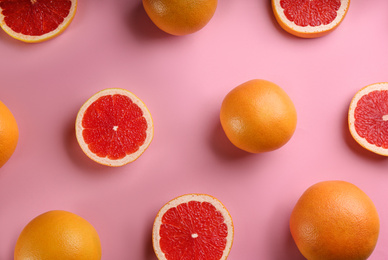 Cut and whole ripe grapefruits on pink background, flat lay