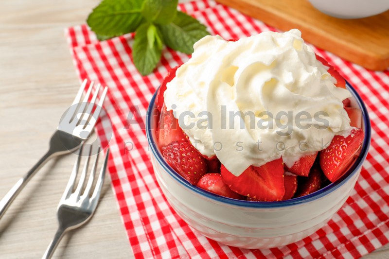 Bowl with delicious strawberries and whipped cream served on wooden table, closeup