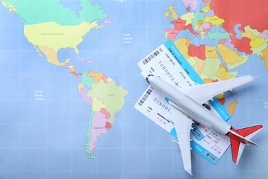 Toy airplane and tickets on world map, flat lay. Travel agency concept