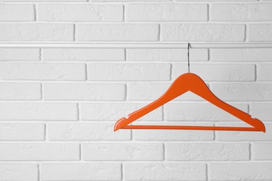 Orange clothes hanger on rail near white brick wall. Space for text