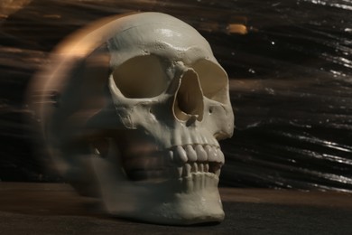 Photo of Human skull with stretch film on stone surface against black background