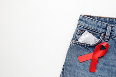 Top view of jeans with condom and red ribbon on white background, space for text. AIDS disease awareness