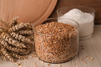 Wheat grains in bowl, spikes and flour on wooden table