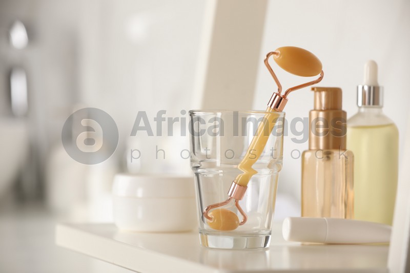 Natural face roller and cosmetic products on shelving unit in bathroom, closeup. Space for text