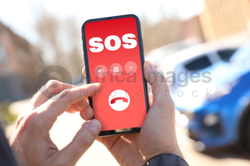Man holding smartphone with emergency call SOS on screen outdoors, closeup