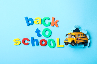 Yellow school bus and phrase "Back to school" on light blue background, flat lay. Transport for students