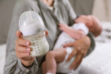 Mother holding bottle of milk and little baby indoors, closeup. Space for text
