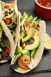 Delicious tacos with shrimps and avocado on black table, closeup