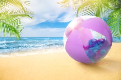 Violet beach ball on sandy coast near sea, space for text 