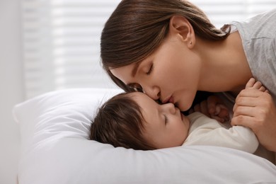 Photo of Happy mother kissing her little baby on bed indoors