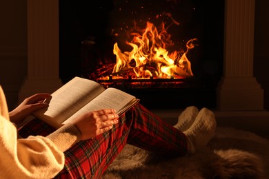Woman with book near fireplace at home, closeup