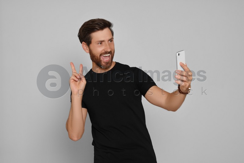 Happy man taking selfie on smartphone against light background