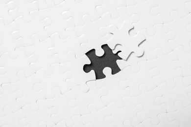 Blank white puzzle with separated piece on black background, top view