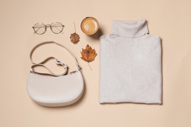 Autumn sweater, bag and eyeglasses on beige background, flat lay