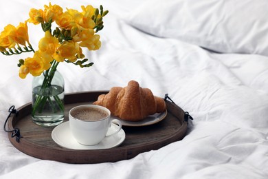 Morning coffee, croissant and flowers on bed, space for text