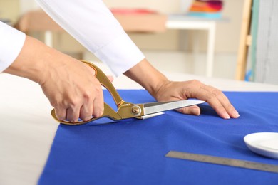 Photo of Seamstress cutting fabric at table in workshop, closeup