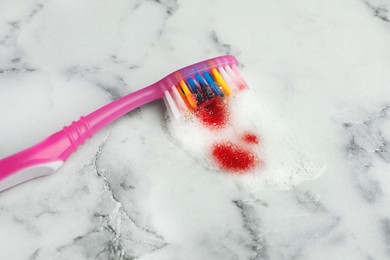 Brush and toothpaste foam with blood on white marble table, closeup. Gum problems
