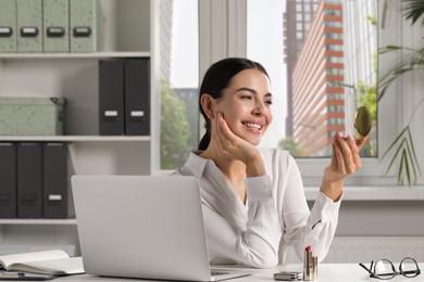 Photo of Young woman looking at cosmetic pocket mirror in office