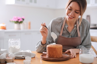 Young woman decorating traditional Easter cake with glaze in kitchen. Space for text