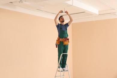 Electrician in uniform with insulating tape repairing ceiling wiring indoors. Space for text