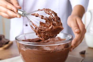 Photo of Professional confectioner whipping chocolate cream with balloon whisk at table, closeup