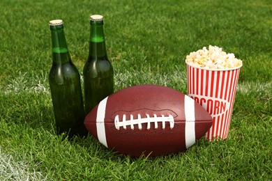 American football ball with beer and popcorn on green field grass