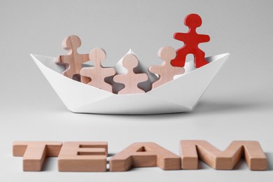 Red figure among wooden ones in paper boat and word Team on white background. Recruiter searching employee
