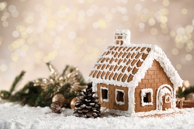 Beautiful gingerbread house decorated with icing on snow against blurred festive lights, space for text