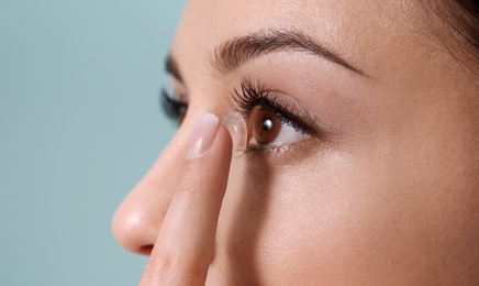 Young woman putting contact lens in her eye on color background