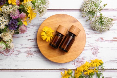 Bottles of essential oils and beautiful flowers on white wooden table, flat lay