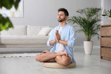 Young man meditating on straw cushion at home