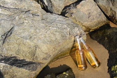 Bottles of cold beer near rocks on sandy beach, space for text