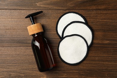 Soap dispenser and makeup remover pads on wooden background, flat lay. Conscious consumption