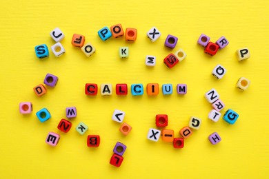 Word Calcium made of colorful plastic beads with letters on yellow background, top view
