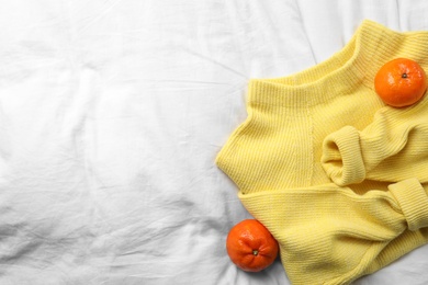 Beautiful yellow warm sweater and tangerines on white bedsheet, flat lay. Space for text