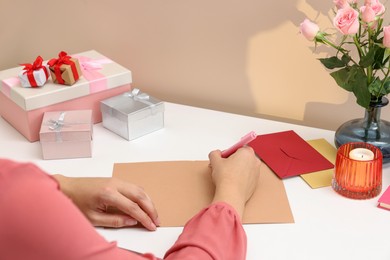 Young woman writing message in greeting card at white table, closeup