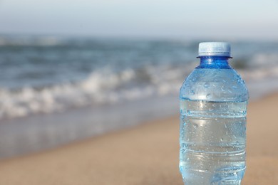 Photo of Plastic bottle of fresh water near sea, closeup. Space for text